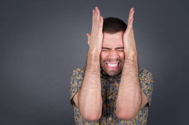 Öfkeli erkek, ellerini şakaklara uzatır, baş ağrısı hisseder, acıdan gözleri kapar, sağlıklı bir uykuya ihtiyacı vardır, aşırı çalışma, yorgunluk ve yorgunluk. Avrupalı adam hasta, gri arka planda izole.