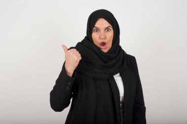 Siyah tesettürlü baygın bayanın yatay görüntüsü parmak ucunda gri arkaplanda izole edilmiş boş bir duvara işaret ediyor. Şuna bir bak. Etnik konsept.