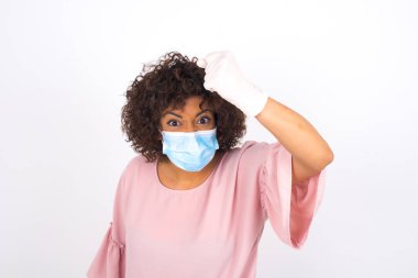 Yüz maskesi takan ve günlük kıyafet giyen bir kadın, beyaz stüdyo arka planında izole edilmiş kızgın bir halde.