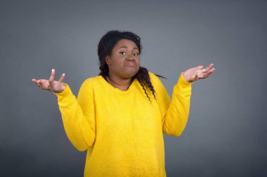 Belki evet ya da hayır. Şüpheli modaya uygun Afrikalı Amerikalı kadın şaşkınlık içinde omuz silkiyor, ne istediğine karar veremiyor beton duvarın üzerinden izole edilmiş. Tereddüt ve belirsizlik.