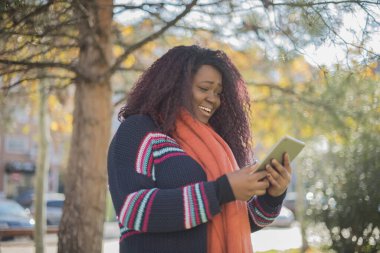 Güz parkında tablet bilgisayar kullanan uzun saçlı, güzel bir Afro-Amerikalı kadın.  
