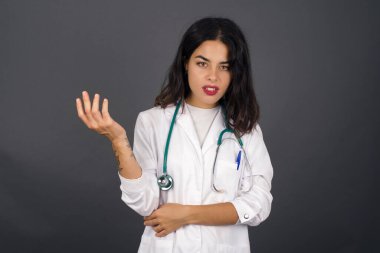 What the hell are you talking about, nonsense. Studio shot of frustrated doctor female gesturing with raised palm, frowning, being displeased and confused with dumb question over gray wall.