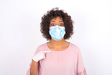 Yüz maskesi takan ve günlük kıyafetler giyen bir kadın beyaz stüdyo arka planında kendini gösteriyordu.