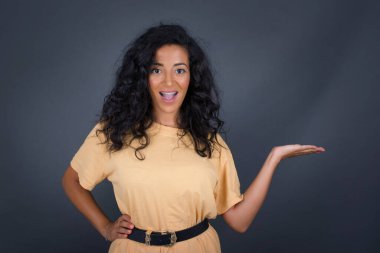 Esmer kadının ifadesine hayran kaldım. Boş alanda bir şeyler gösteriyor. Açık elle izole edilmiş gri arka planı var. Reklam kavramı.