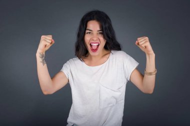 Sıradan tişörtler giyen, kollarını kaldıran, yumruklarını sıkan, sevinç ve heyecanla haykıran güçlü ve kararlı genç bir kadının portresi. Zafer, başarı ve başarı kavramı. 