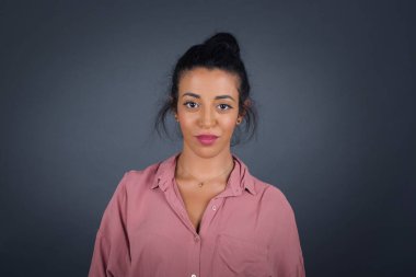 Stüdyoda, siyah saçlı güzel bir kadının hoş bir gülümsemeyle kameraya bakarken içeriğiniz için gri boş fotokopi duvarına poz verirken yakın çekim.