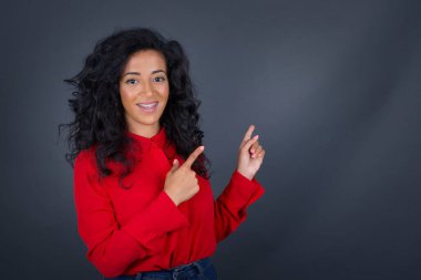 Kıvırcık saçlı, kırmızı tişörtlü güzel esmer kadın promosyon metniniz veya reklamınız için ön parmakları boş fotokopi alanında olduğunu gösteriyor..