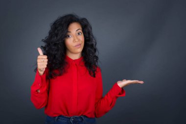 Kıvırcık saçlı, kırmızı tişörtlü genç esmer kadın başparmağını kaldırıyor ve diğer eliyle dışarıda dikiliyordu..