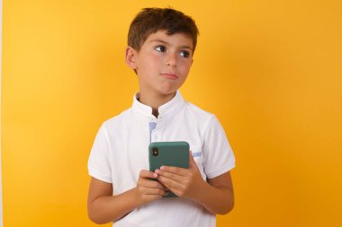 Sarı duvarda akıllı telefonu olan sevimli çocuk.  