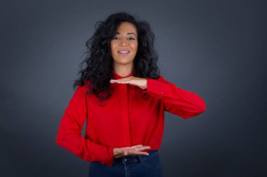 Kıvırcık saçlı, kırmızı gömlekli genç esmer kadın büyük ve büyük beden işareti gösteriyor, ölçü sembolü. Kameraya bakıp gülümsüyor. Ölçüm konsepti.