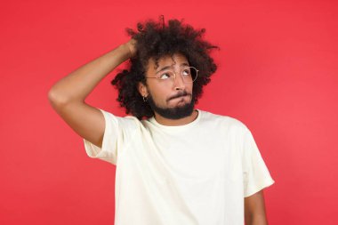 Afro saçlı genç adamın kırmızı duvara karşı kafası karışık. 