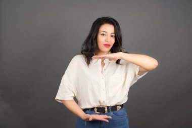 Güzel esmer kadın bir şey gösteriyor. Gri arkaplanda duruyor. 