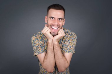 Mutlu bir adamın stüdyo fotoğrafı, çenesinin altında el ele tutuşur, keyifli bir ruh hali içindedir, ertesi gün için arkadaş fikrini sever, gri duvarda izole edilmiş..