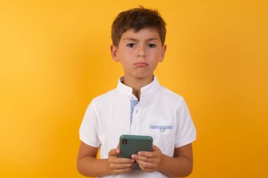 Akıllı telefonu sarı duvara dayayan sevimli çocuk.  