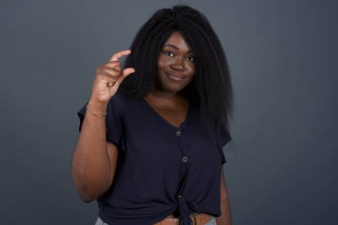 Afrikalı Amerikalı kadın izole edilmiş, el hareketleriyle küçük boy, ölçü sembolü gösteriyor. Kameraya bakıp gülümsüyor. Ölçüm konsepti.