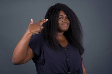 Mutsuz Afrikalı Amerikalı kadın silah atışı taklidi yapıyor intihar jesti yapıyor iki parmağını şakakların üstünde tutuyor günlük kıyafetleri giymiş şaşkın ifade içeride duruyor.. 