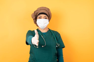 Stetoskop ve yüz maskeli kadın doktor stüdyoda el ele veriyor.