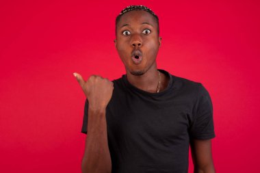 Genç ve neşeli afro-amerikalı bir adamın başparmağıyla işaret ettiği yatay çekim arka planda izole edilmiş boş bir duvara işaret ediyor. Şuna bir bak. Etnik konsept.
