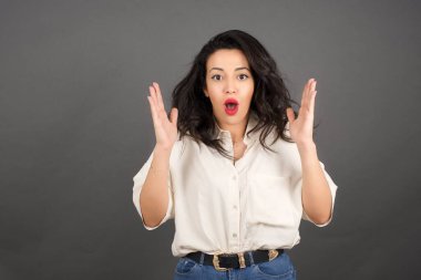 Gayri resmi giyinmiş güzel esmer kadının kafası karışmış. Gri arkaplanda duruyor.  