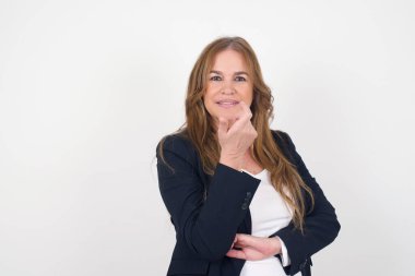 Yüzüne yakın eli olan, şüpheli ve şüpheci bir ifadeyle kameraya bakan, şık, orta yaşlı, beyaz bir kadının izole edilmiş portresi. Gri arkaplan üzerinde izole.