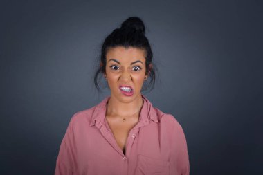 Deli kadın dişlerini öfkeyle sıkar, gelen sesten rahatsız olur, şık kıyafetler giyer, gri arka planda izole olur..