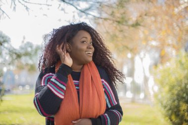 Uzun kıvırcık saçlı, renkli süveter giyen güzel Afro-Amerikan kadın parkı dinliyor.  