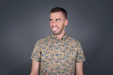 Hayalperest genç bir erkek, düşünceli bir yüz ifadesi var, elleri havada, dudaklarını ısırıyor, gri duvara karşı hoş bir poz düşünüyor..