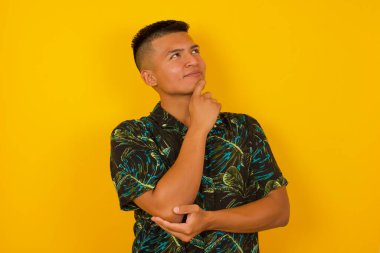 Düşünceli gülümseyen bir adamın portresi elini çenesinin altında tutar, yan bakar, ilginç bir şey düşünür ya da merak eder, sıradan giyinir, sarı stüdyoya karşı poz verir..