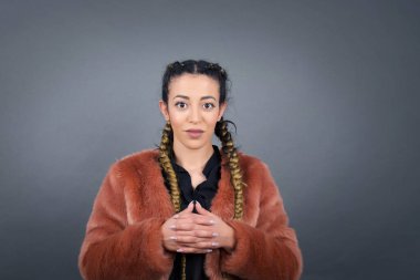 Gri arka planda, kendine güvenen yüzüyle el ele tutuşan güzel bir kadın portresi..