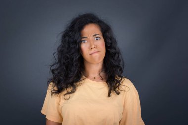 Düşüncelere dalmış, kaşlarını kaldırmış, dudaklarını kıvırmış, şık kıyafetler giymiş, metnin için gri duvarın karşısında duran çekici esmer kadın..