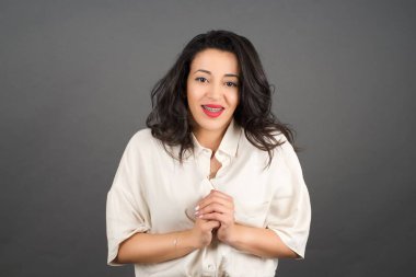 Güzel esmer kadın gülümsüyor. Gri arkaplanda duruyor. 