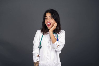 Şaşırtıcı güzellikteki doktor kız. Yakın plan portre kadın doktor, ağzı açık, ağzı açık, eli yüze yakın bir şekilde şaşırmış görünüyor. Olumlu duygu yüz ifadesi vücut dili.