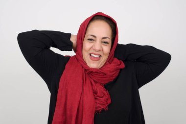 Güven ve cinsel ilişki konsepti. Çekici, olgun Müslüman bir kadının portresi, kendinden emin bir ifadeyle gülümseyen ve ellerini başının üstünde tutan. Gri arkaplanda duruyor.