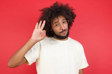 Afro saçlı genç adam kırmızı duvara üç parmak gösteriyor. 