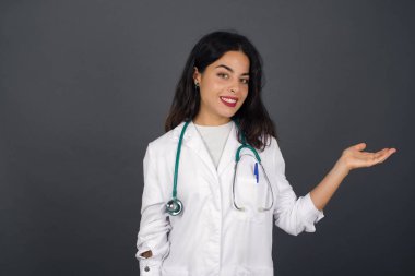 Pozitif memnun doktor diyor ki: Vay be, ne kadar heyecan verici, hayret verici bir ifade, boş alanda bir şey gösteriyor, açık elle izole edilmiş gri arkaplan üzerinde. Reklam kavramı.