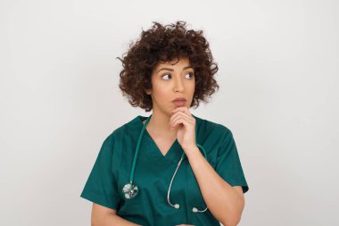 Düşünceli, düşünceli, genç bir doktor kadın elini çenesinin altında tutuyor, düşünceli görünüyor.