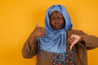 Genç, dalgın, Afro-Amerikan Müslüman kadın iyiye-kötüye işaret veriyor. Sıradan kıyafetler giymekten memnun değil ve etkilenmiyor..