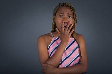 Gri arka plandan korkan genç Afrikalı Amerikalı kadın eliyle ağzını kapatıyor.