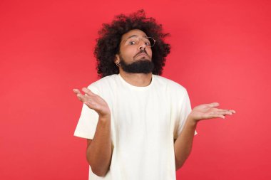 Afro saçlı genç adamın kırmızı duvara karşı kafası karışık. 