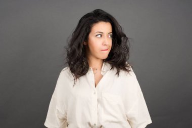 Güzel esmer kadın, sıradan giyinmiş, gri arka plana bakıyor..  