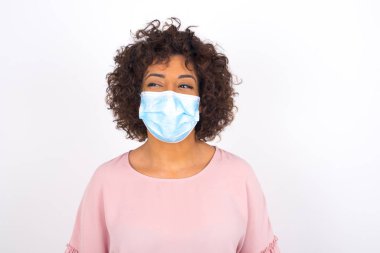 Yüz maskesi takan ve beyaz stüdyo arka planında izole edilmiş günlük kıyafetler giyen bir kadın.