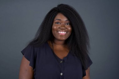 Gülümseyen mutlu ve komik yüzlü güzel Afrikalı Amerikalı kadın. Günlük giysiler giyip gri stüdyonun arka planında dikiliyorlar..