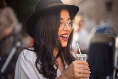 Sokakta elinde içkiyle gülümseyen güzel esmer kadın. 