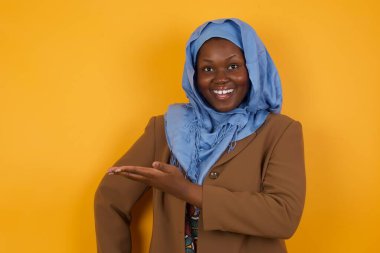 Afro-Amerikan Müslüman kadın diyor ki: Vay be, ne kadar heyecan verici, hayret verici bir ifade, boş alanda izole edilmiş sarı arka planda bir şey gösteriyor. Reklam kavramı. 