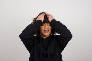 Öfkeli kadın ellerini başının üstüne koyuyor, baş ağrısı çekiyor, gözleri acıdan kapanıyor, sağlıklı bir uykuya ihtiyacı var, aşırı çalışma, yorgunluk ve yorgunluk. Avrupalı kadın hasta, gri arka planda izole edilmiş.