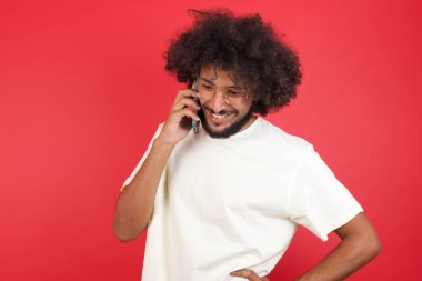 Kızıl duvara karşı akıllı telefondan konuşan afro saçlı genç adam.   