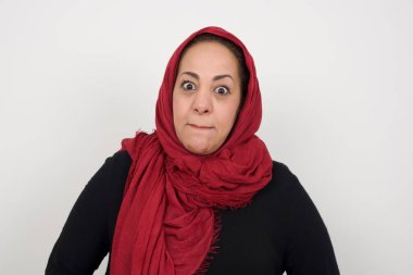 Şaşırmış olgun Müslüman kadının fotoğrafı dudaklarını kıvırıyor ve endişeli bir bakış atıyor, önünde korkunç bir şey görüyor, beyaz arka planda izole edilmiş.