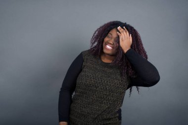 Mutlu, genç, Afro-Amerikalı kadın, günlük giysiler içinde, pozitif gülümseyen, uzun saçlı, haftasonu tatilinden memnun ve yorucu bir haftadan sonra dinlenen, gri duvarda izole edilmiş..