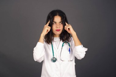 Hayalperest beyaz doktor, düşünceli bir yüz ifadesi var, yüzünü çevirmiş, hoş bir şeyler düşünüyor, gri duvara karşı poz veriyor..