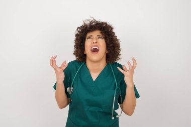 Çığlık, nefret, öfke. Mavi stüdyo arka planında çığlıklar atan, tıbbi üniforma giyen, ağlayan, sinirli, güzel Arap doktor kadın. Duygusal, genç yüz. İnsani duygular, yüz ifadesi kavramı.